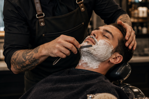 a man sitting in a barber's chair getting a hot lathering shave from the barber